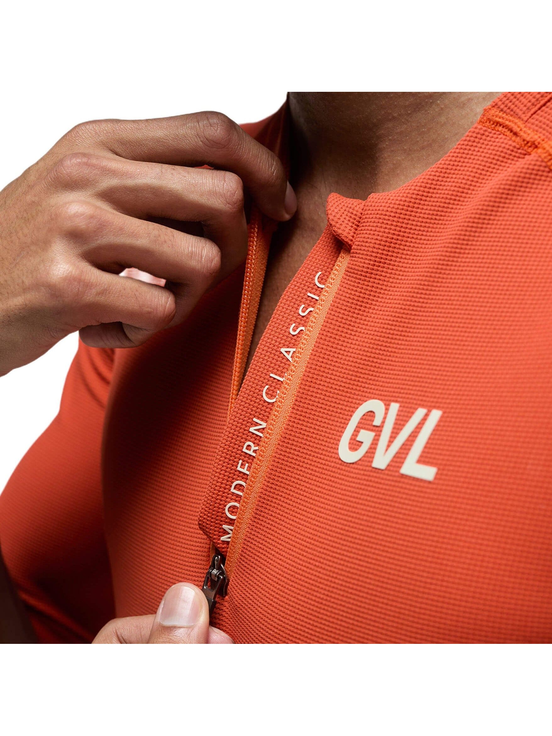 Close-up of the chest area of a Givelo Modern Classic half-zip jersey in a vibrant pumpkin color. The image shows the texture of the waffle fabric, the neatly crafted zipper, and the bold 'GVL' branding on the right side.