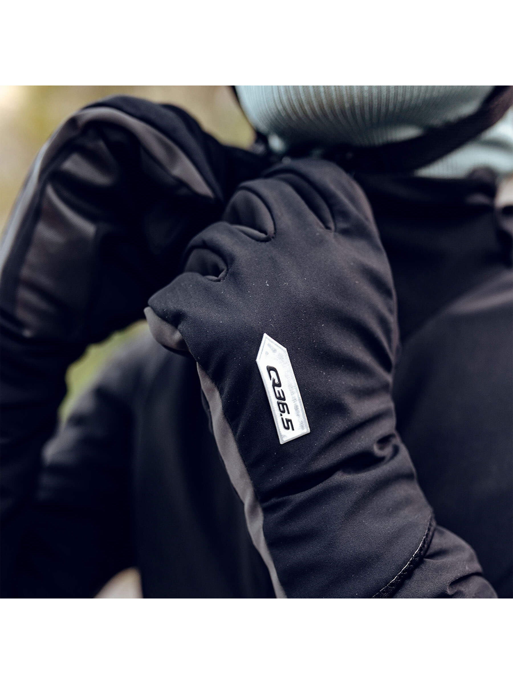 Cyclist adjusting helmet while wearing the Q36.5 Hybrid Que X Gloves in black.