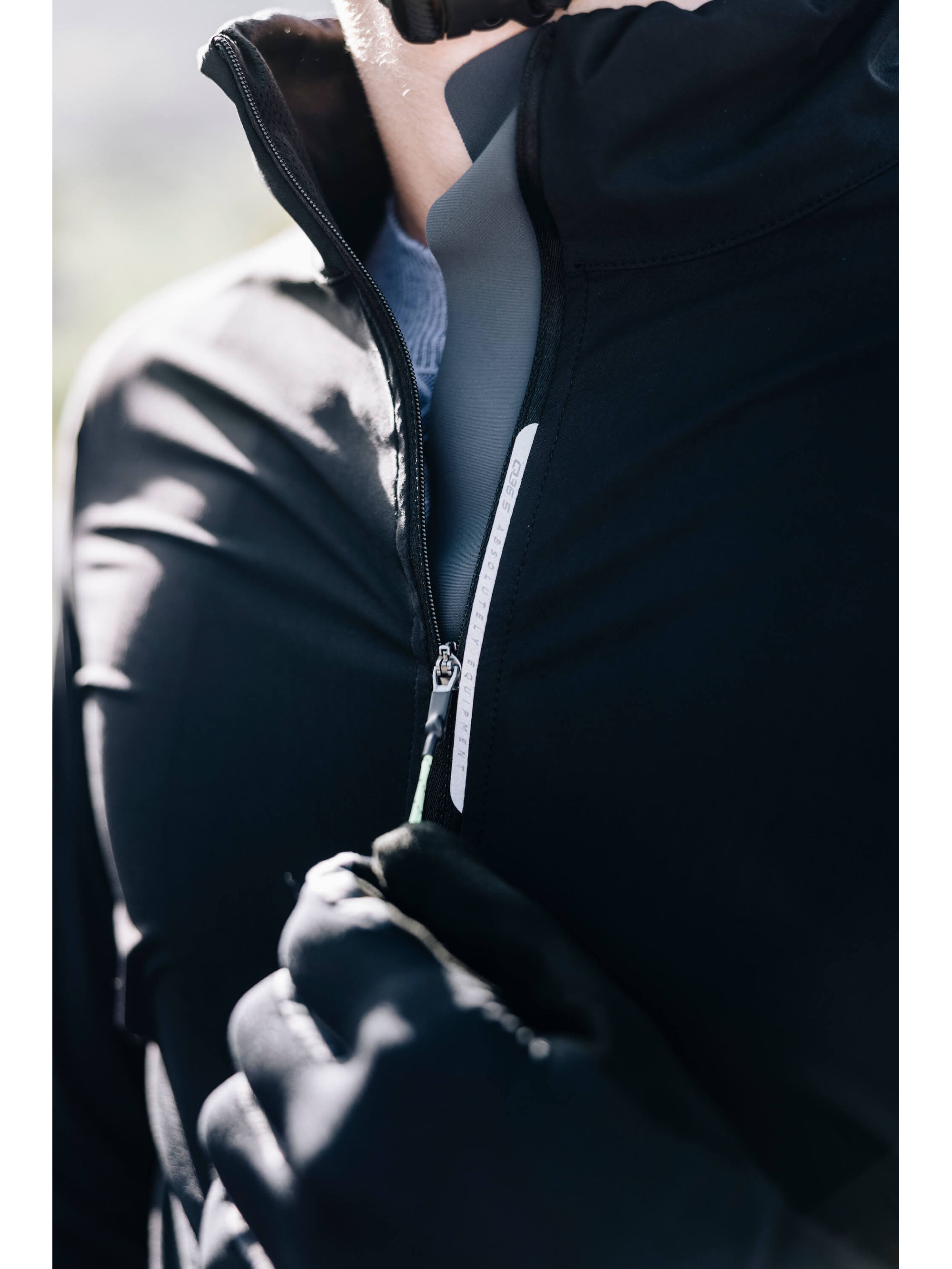 A cyclist zipping up the black Q36.5 Bat Shell Jersey, emphasizing the weatherproof and moisture-preventing properties of the fabric.