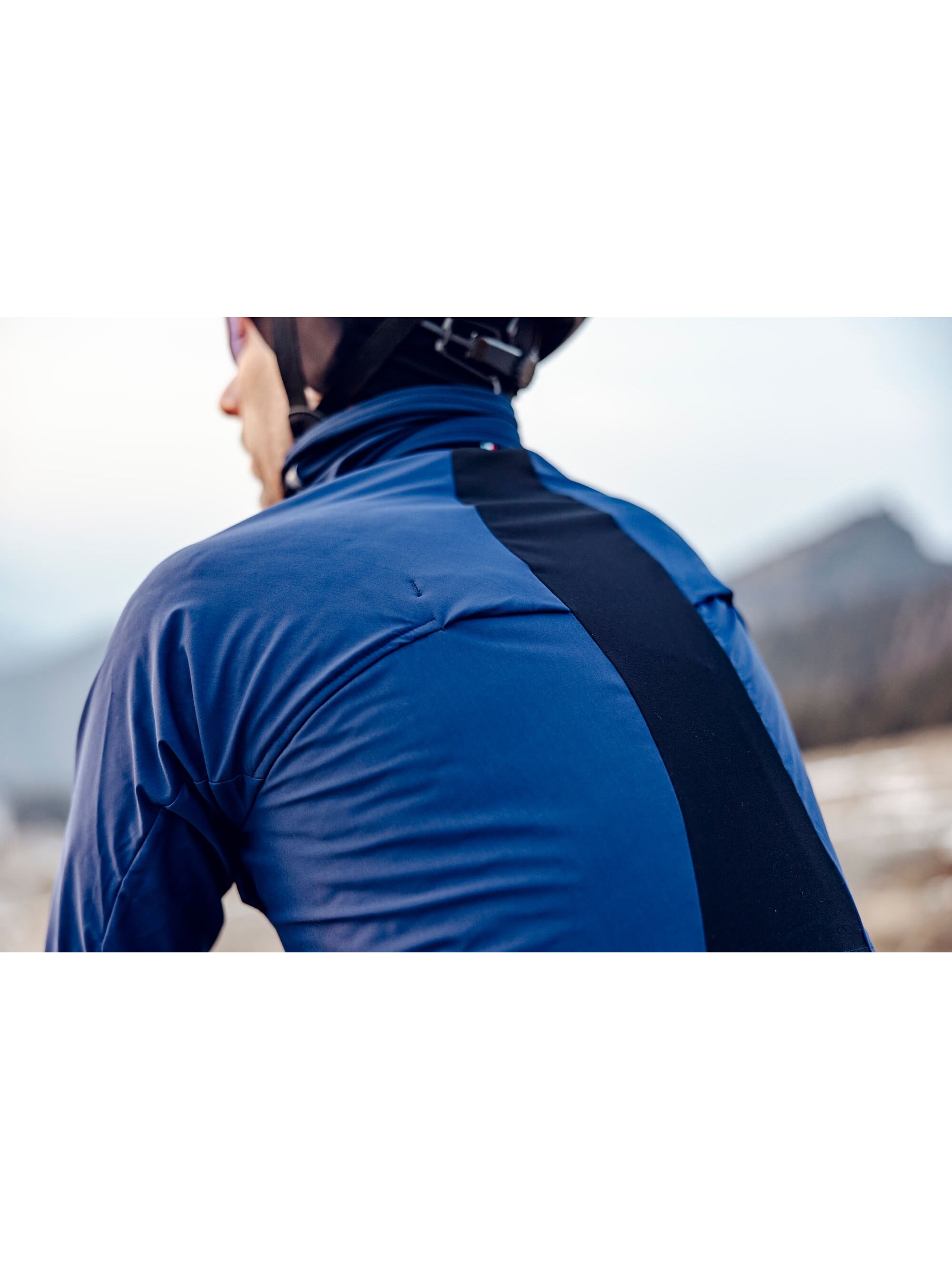 Rear perspective of a cyclist wearing the Q36.5 Bat Jacket in navy, showcasing the strategic ventilation openings for moisture control.