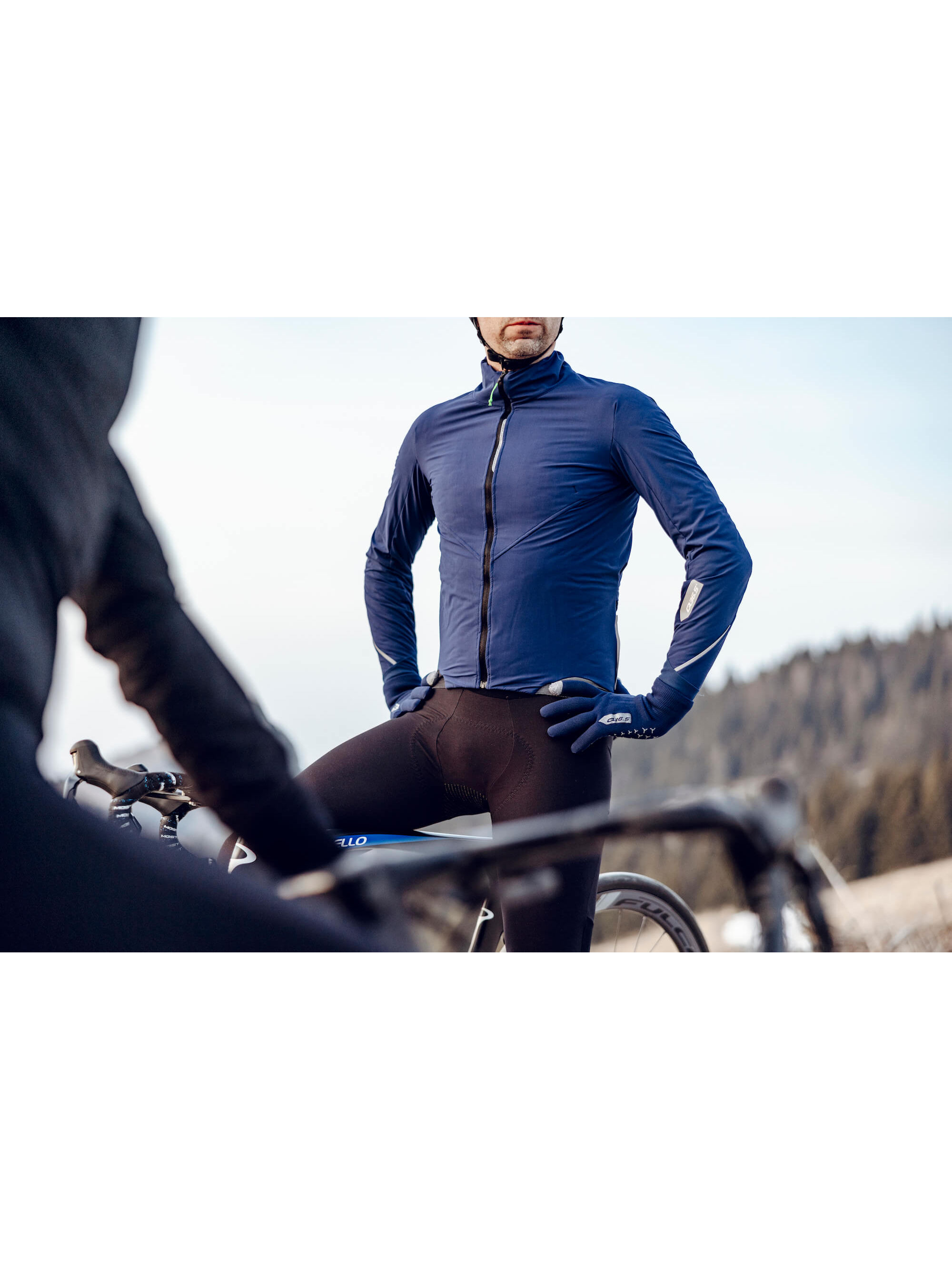 A cyclist posed with the Q36.5 Bat Jacket in navy, demonstrating the fit and utility with three traditional back pockets for essentials.