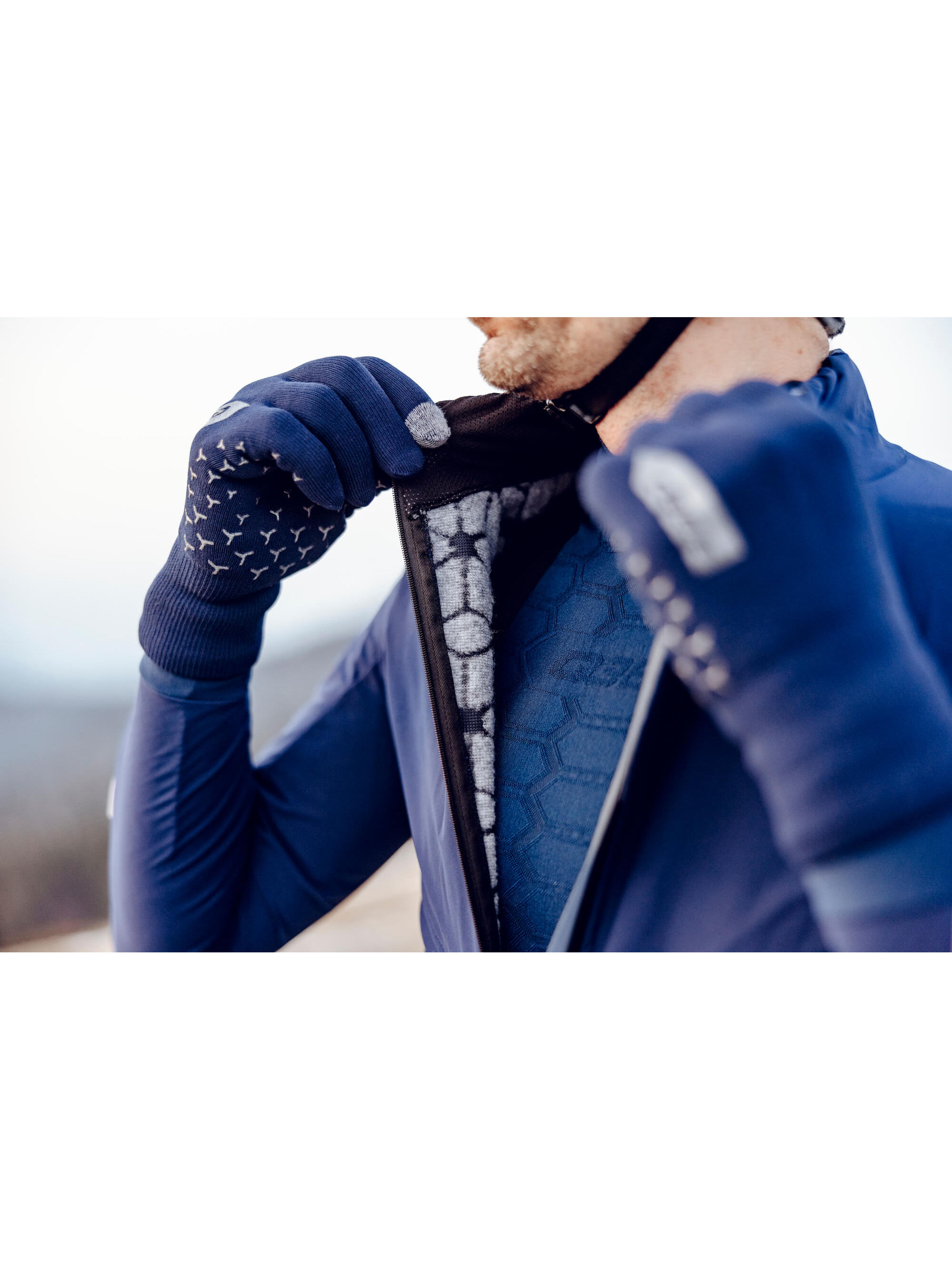Close-up of a cyclist adjusting the hermetic collar on the Q36.5 Bat Jacket in navy, indicating the weatherproof and comfort features.