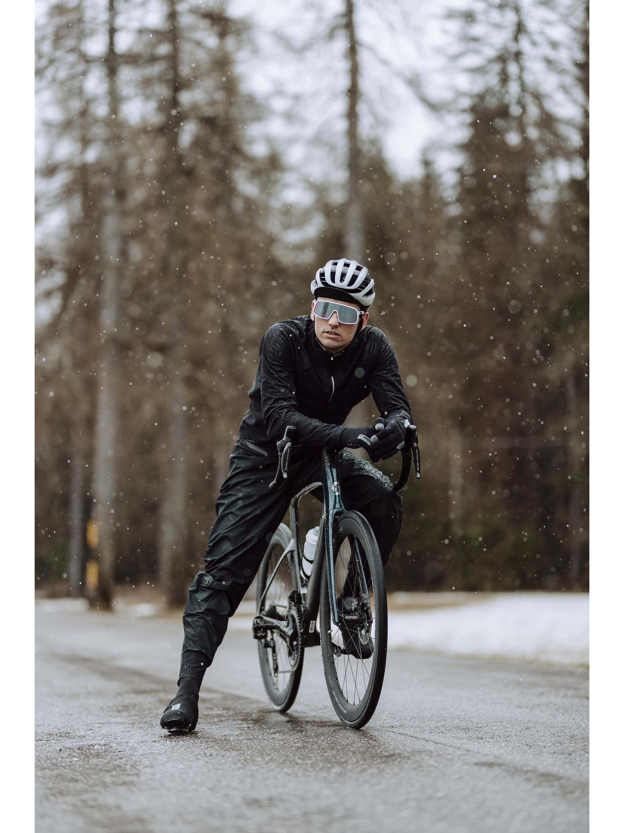 Cyclist wearing Q36.5 Rain Overpants in wet conditions, demonstrating visibility and protection.