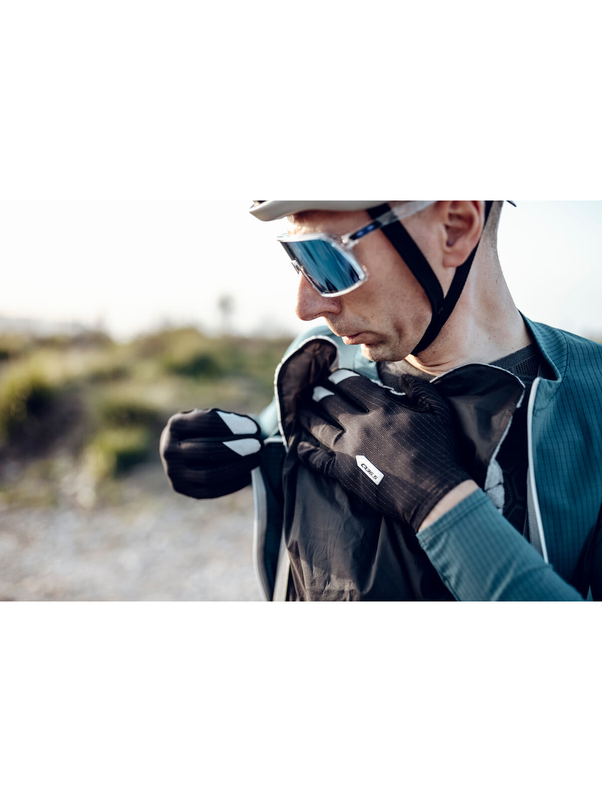 A cyclist adjusting the black Q36.5 Wind Shell over the shoulder, demonstrating its practicality and ease of use during outdoor activities.