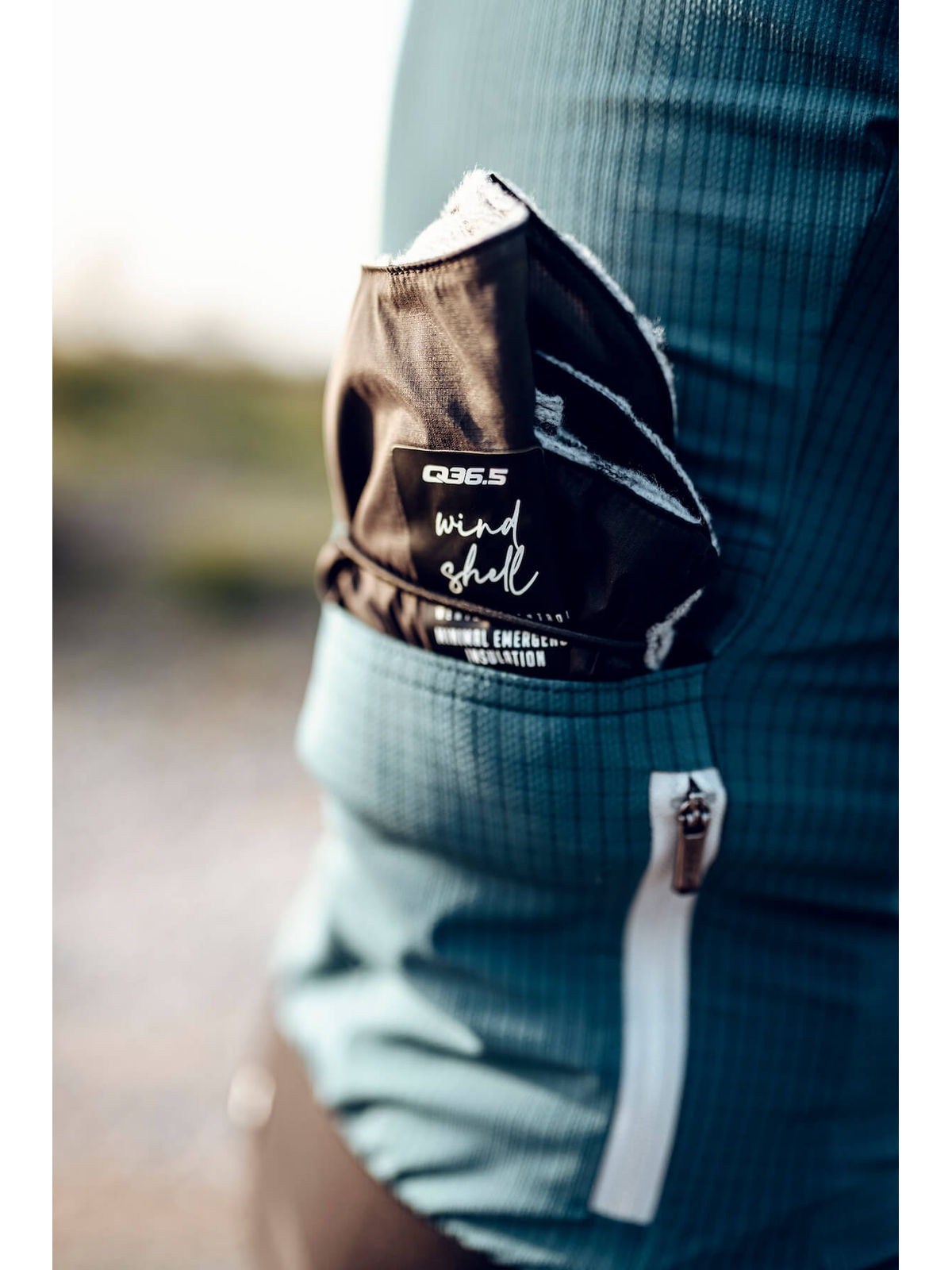The Q36.5 Wind Shell tucked into the back pocket of a cyclist's jersey, showing its portability and accessibility for on-the-go use.