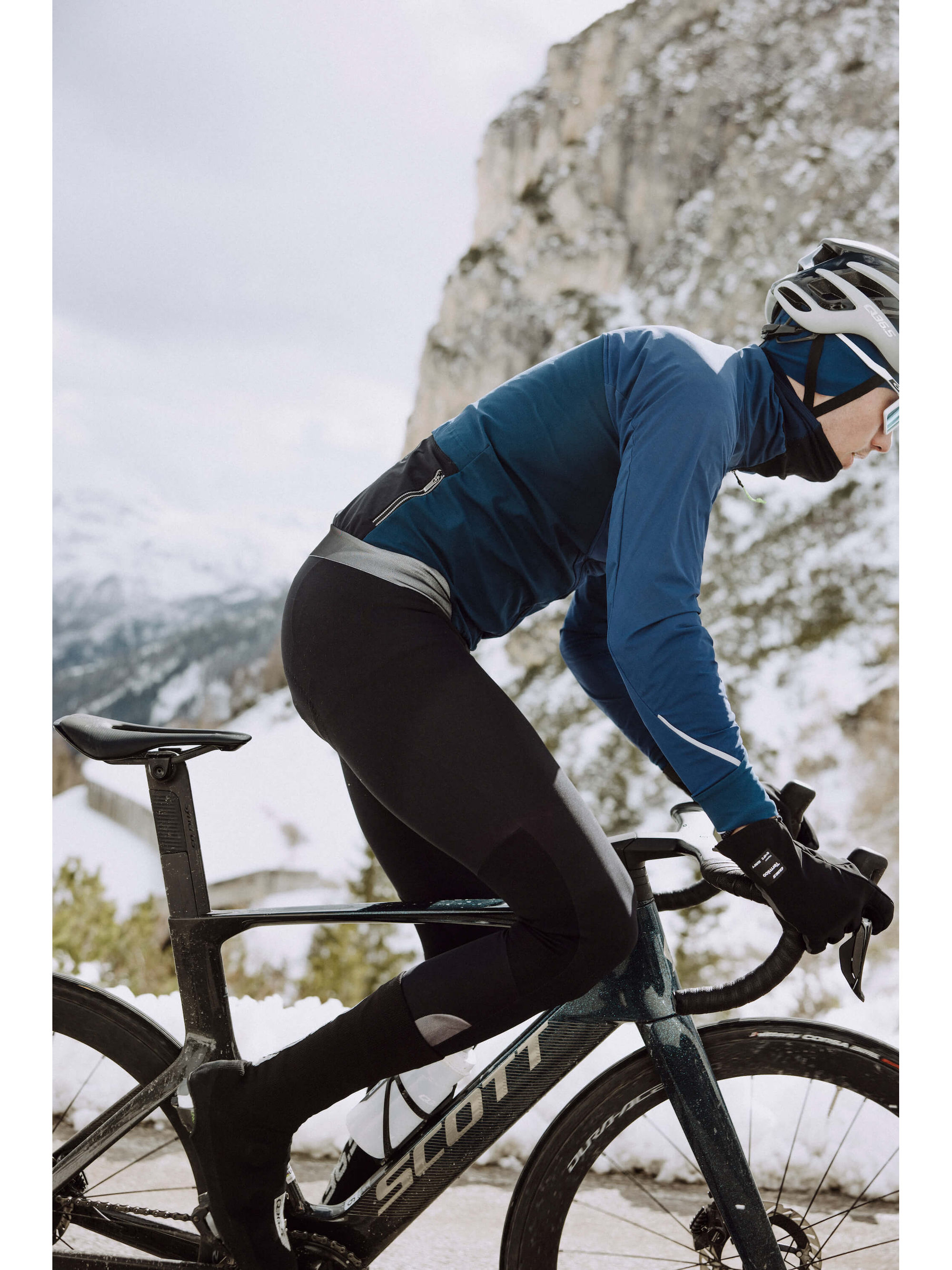 Cyclist in Q36.5 Winter Bib Tights riding in snowy conditions with mountain backdrop.