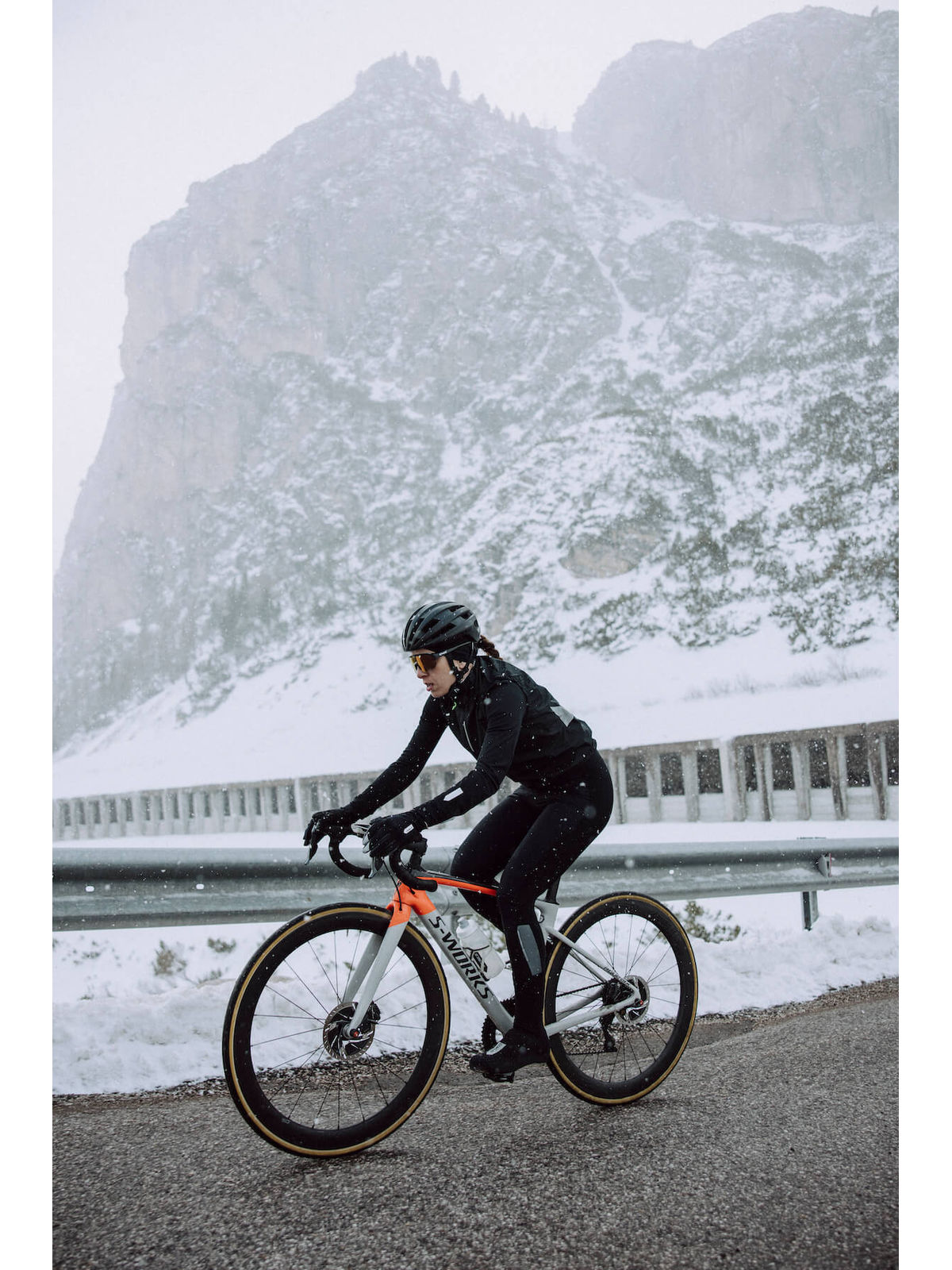 A cyclist in motion wearing Q36.5 Winter Bib Tights, illustrating the ergonomic fit and comfort during a snowy mountain ride.