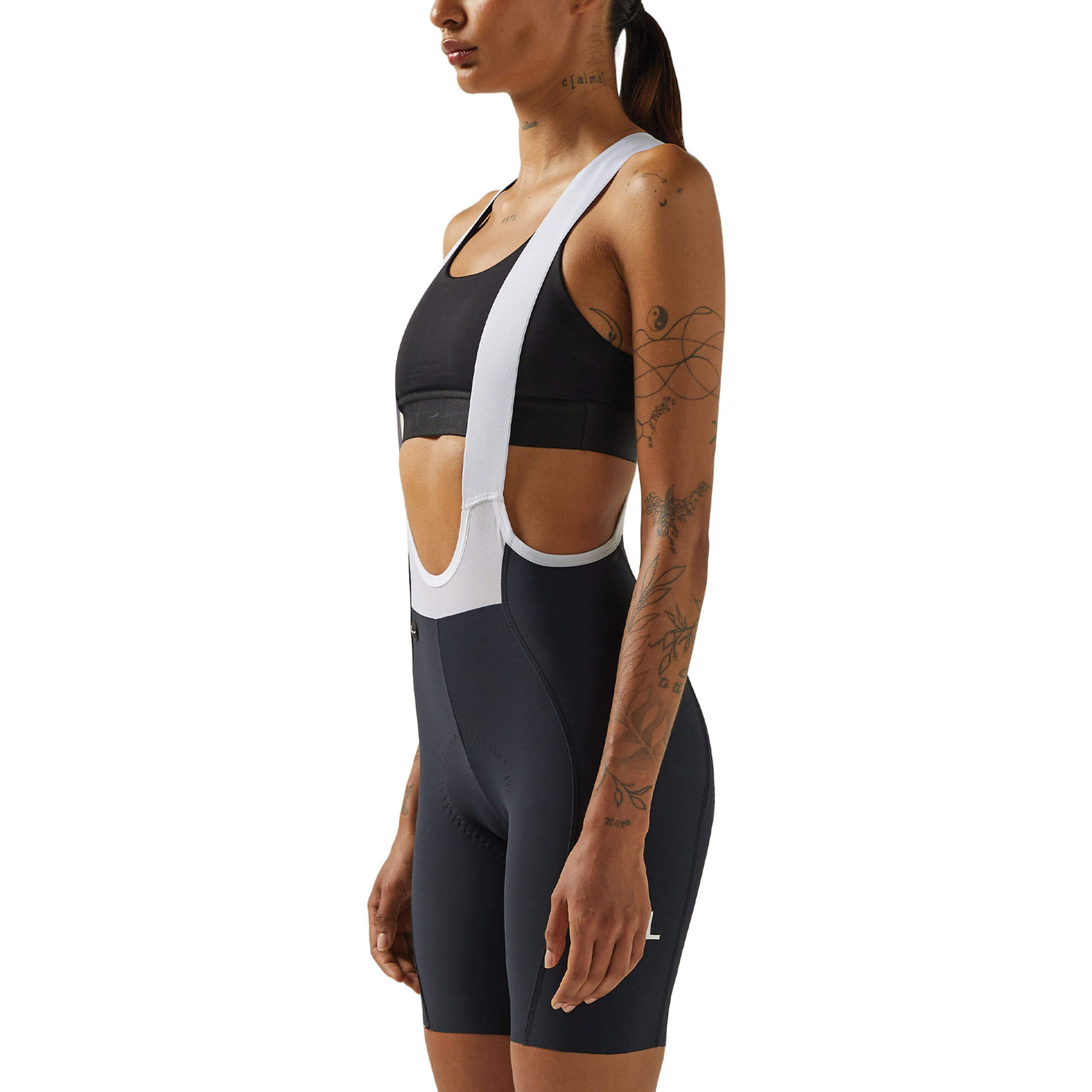 A woman in a side view wearing black Givelo HD Pro Bib Shorts and a white mesh vest. The shorts are designed with attention to comfort for extensive cycling, showcasing the compression and fit that aids in long-duration rides.