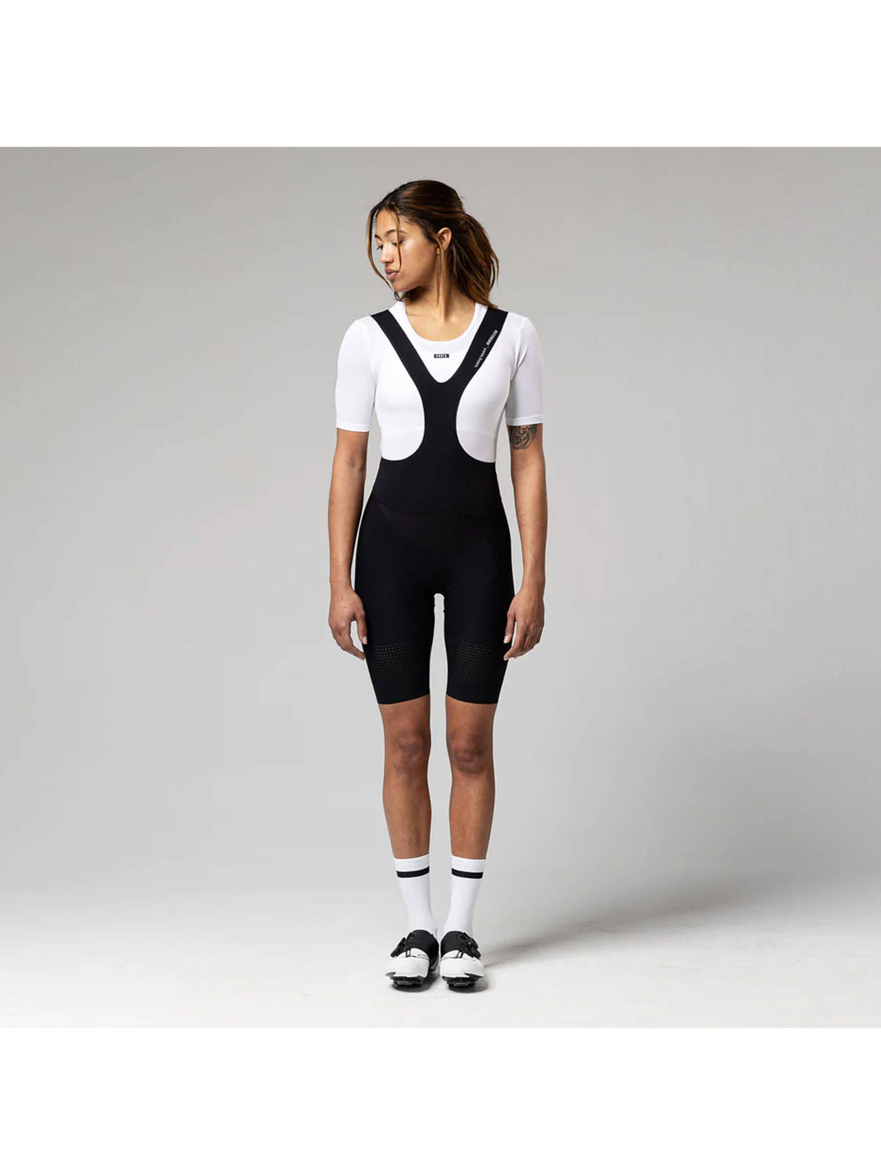 A woman in a contemplative pose wearing the GOBIK women's short-sleeved base layer, showing the snug fit and mesh ventilation zones for cooling.