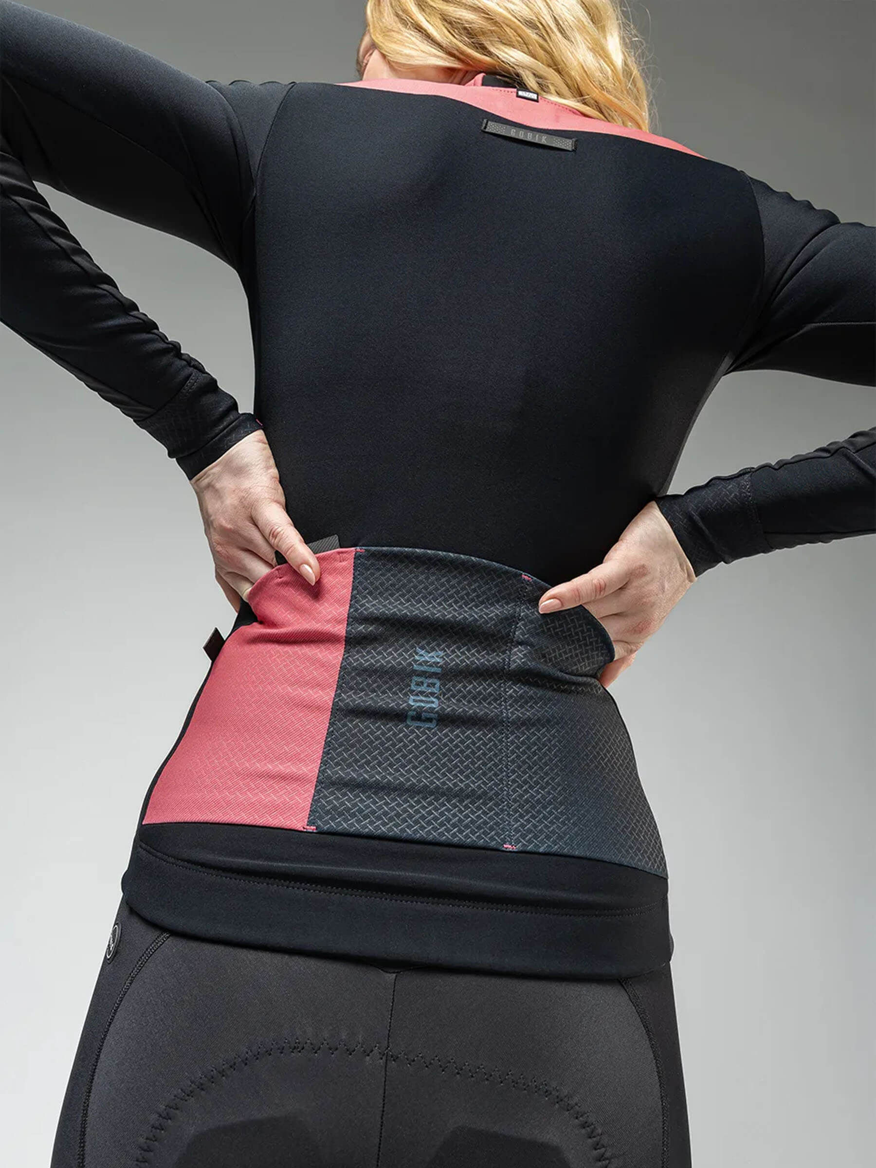 A woman in a pink and black cycling jersey, featuring the Women's Jacket: MIST BLEND 2.0, designed for peak performance and protection.